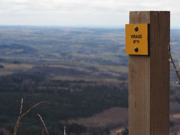 Close-up of road sign on wood against sky