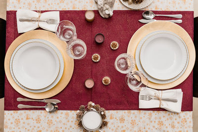 Top view of table setting with glasses and cutlery near plates decorated with candles and cones for christmas celebration