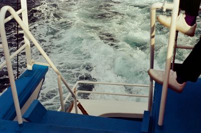 Low section of person standing on railing in ship