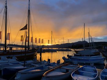 Sailboats moored in harbor at sunset