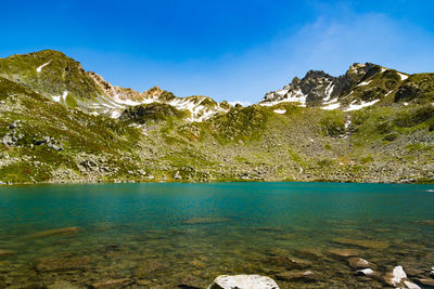 Scenic view of lake by mountains against blue sky