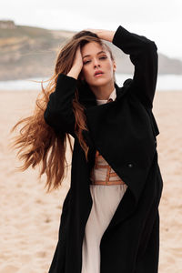 Woman with dress and harness at the beach on a windy day holding her hair, portugal