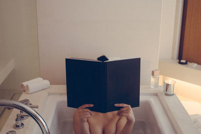 Midsection of woman reading book in bathtub