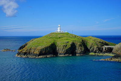 Lighthouse amidst sea and buildings against sky