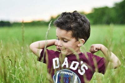 Cute boy flexing muscles while standing amidst plants on field