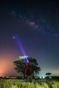 Rear view of man flashing light at sky on field