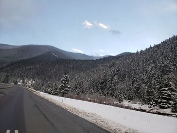 Snow covered road by mountains against sky