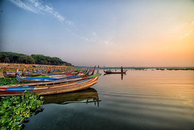 Boats moored in sea against sky during sunset