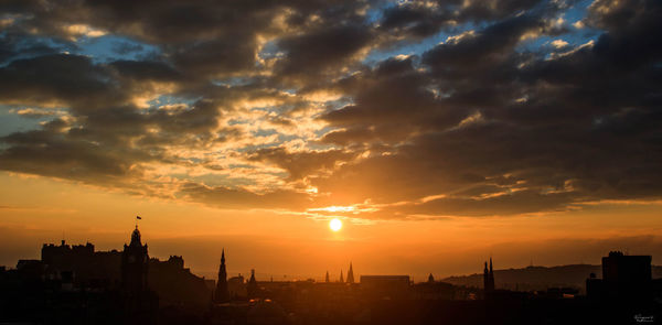 Silhouette buildings against cloudy sky during sunset