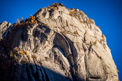 Low angle view of rocky mountains against clear blue sky