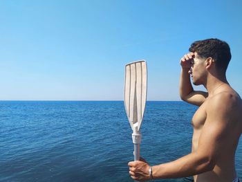 Young man standing in sea against clear blue sky