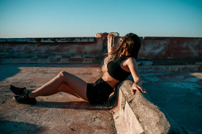 Side view of woman sitting on floor against clear sky