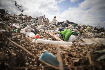 Low angle view of people at junkyard against cloudy sky