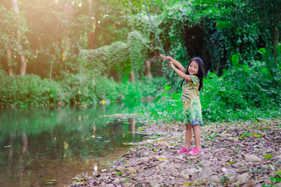 Cute girl smiling holding rope swing while standing by lake