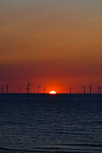 Silhouette wind turbines on land against sky during sunset