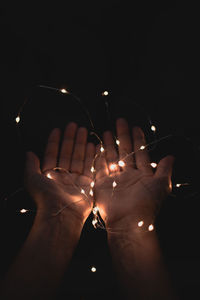 Close-up of hand holding illuminated lighting equipment against black background