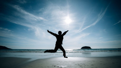 Full length of silhouette woman jumping at beach against sky