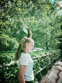 Young woman standing by plants against trees