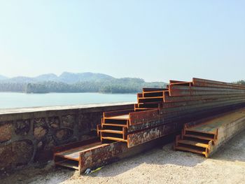 Stack of girders by lake against sky