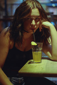 Portrait of young woman drinking juice on table