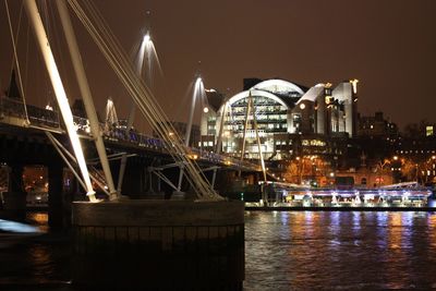 Illuminated bridge over river against sky at night