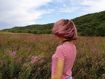 Side view of mid adult woman with short hair standing on grassy field against sky