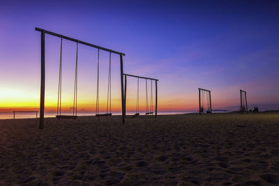 Swings at beach against sky during sunset