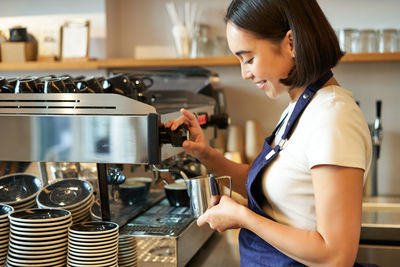 Side view of young woman holding coffee at home