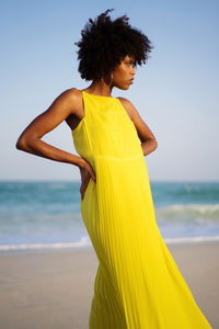 Low angle shot beautiful black woman with afro wearing yellow dress against blue sky