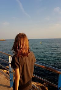 Rear view of girl looking at sea while standing against sky