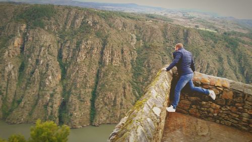 Full length of man looking down while standing at observation point against mountain