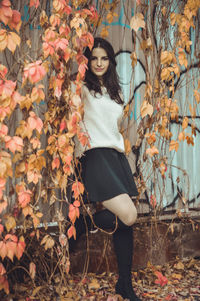 Portrait of young woman standing amidst creeper plants during autumn