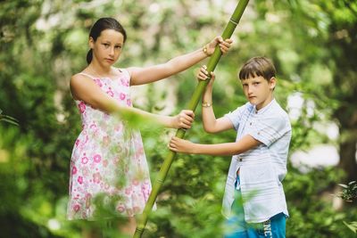 Siblings standing on tree against plants