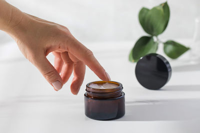 A woman's hand reaches for a jar of nourishing skin cream on a white background 