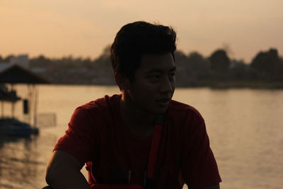 Portrait of young man standing against lake during sunset