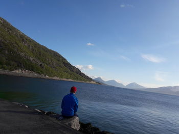 Rear view of man looking at mountains against blue sky