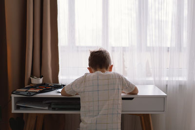 Cute kid boy studying at home and doing school homework. thinking child sitting at table.