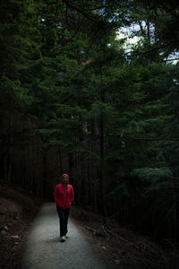 Woman wearing hooded jacket standing on tree at forest