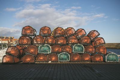 Stack of fishing net on land by sea against sky