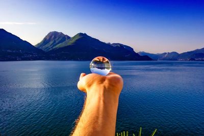 Close-up of hand holding sea against mountains