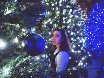 Portrait of young woman with christmas tree at night