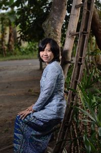 Portrait of smiling young woman sitting on ladder outdoors