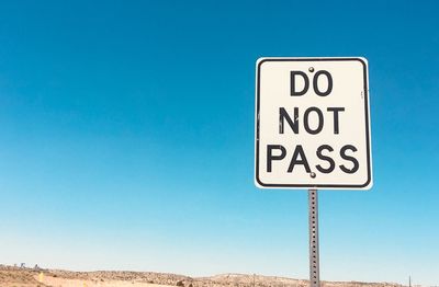 Low angle view of road sign against clear blue sky