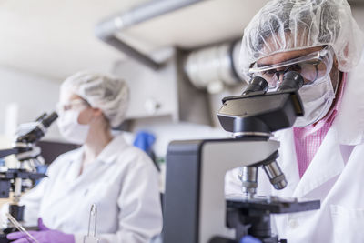 Man and woman scientists looking through microscope at laboratory