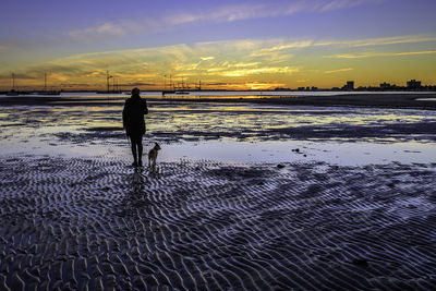 Silhouette man walking on beach against sky during sunset