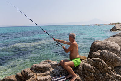 Fisherman sitting on a rock and fishing with a rod