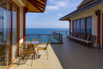 Empty chairs and tables at restaurant by sea against sky