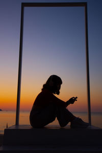 Silhouette man using mobile phone against sky during sunset