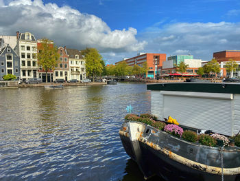 Boats in river by buildings in city against sky