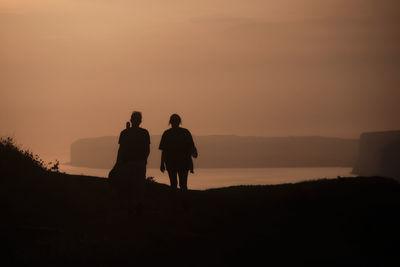 Rear view of silhouette men standing against sky during sunset